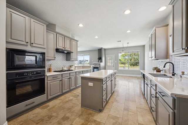 kitchen with gray cabinetry, a kitchen island, under cabinet range hood, black appliances, and a sink