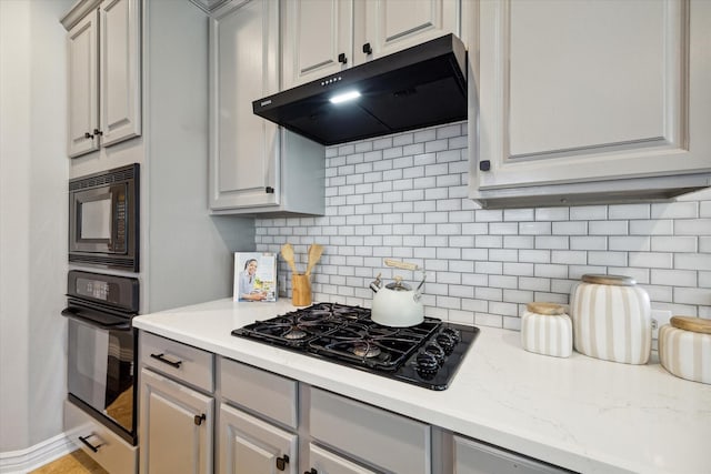 kitchen featuring tasteful backsplash, gray cabinetry, extractor fan, light stone countertops, and black appliances