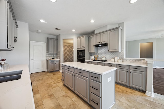 kitchen featuring under cabinet range hood, gray cabinetry, black appliances, and a center island