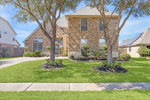 view of front facade featuring a front lawn, fence, brick siding, and roof with shingles