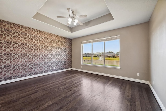 empty room with ceiling fan, baseboards, a raised ceiling, and dark wood finished floors