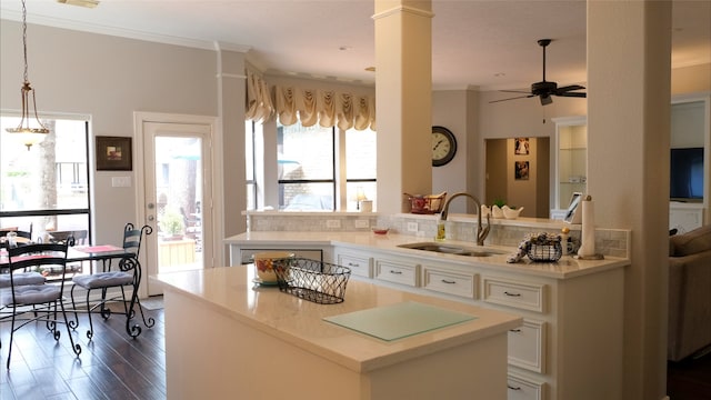 kitchen with white cabinets, ornamental molding, a kitchen island, and a sink