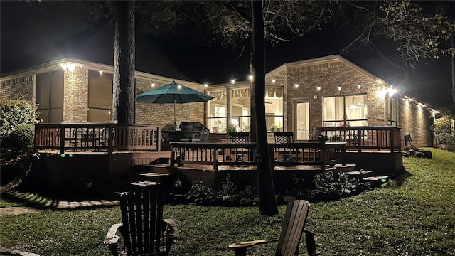 back of house at night with a wooden deck and brick siding