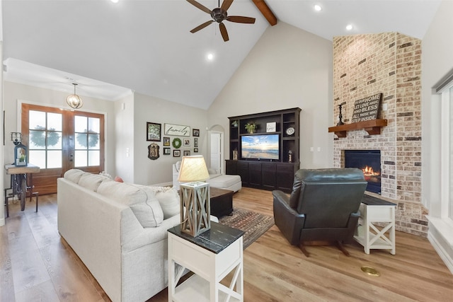 living room with beam ceiling, high vaulted ceiling, french doors, light wood-style floors, and a brick fireplace