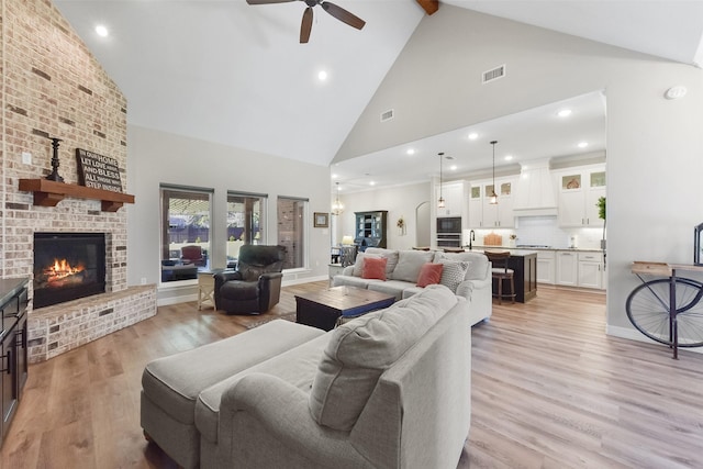 living area with a ceiling fan, visible vents, light wood finished floors, high vaulted ceiling, and a fireplace