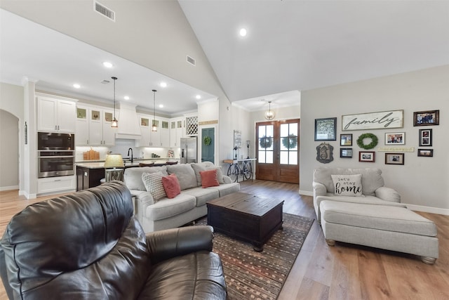 living area featuring visible vents, high vaulted ceiling, light wood-style flooring, french doors, and arched walkways