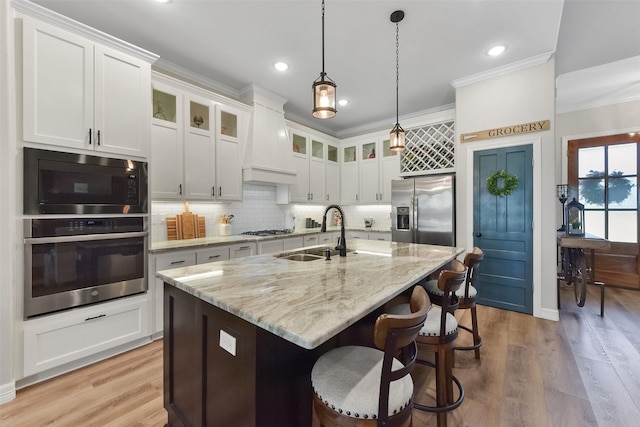 kitchen with ornamental molding, a sink, tasteful backsplash, stainless steel appliances, and light wood-style floors