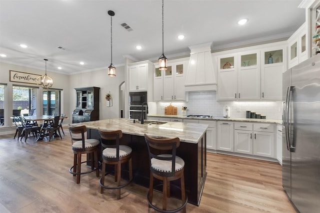 kitchen with custom range hood, light stone counters, light wood-style floors, stainless steel appliances, and a sink