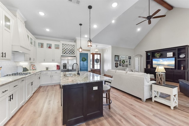 kitchen with beamed ceiling, light wood-type flooring, arched walkways, stainless steel appliances, and a sink