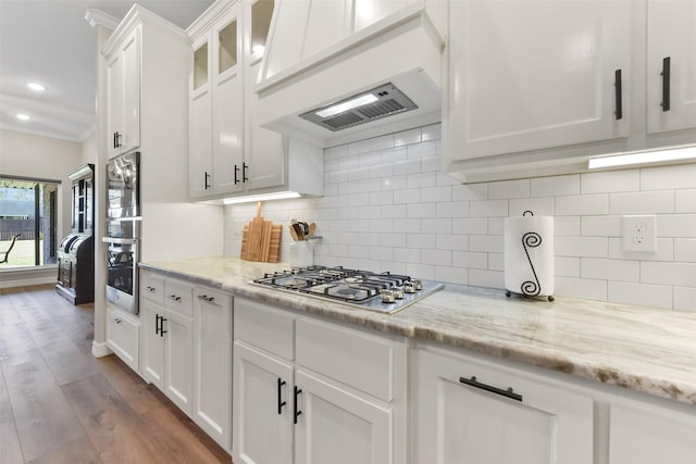 kitchen with glass insert cabinets, ornamental molding, appliances with stainless steel finishes, wood finished floors, and white cabinetry