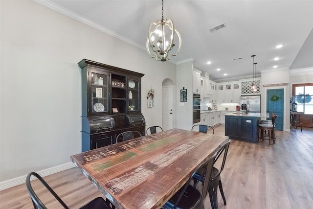 dining room with visible vents, crown molding, baseboards, light wood-style flooring, and arched walkways