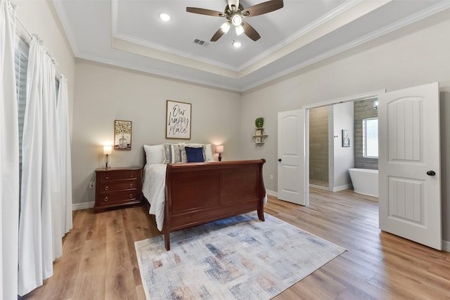 bedroom featuring baseboards, a raised ceiling, light wood-style floors, and crown molding