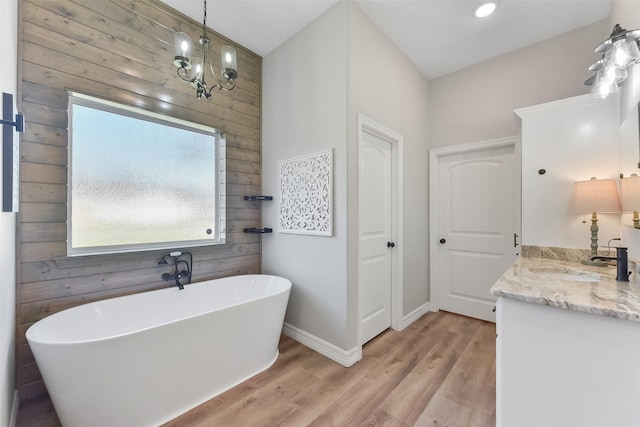 full bath with wood finished floors, an inviting chandelier, baseboards, a freestanding bath, and vanity