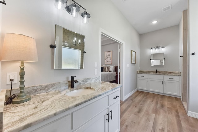 bathroom with two vanities, wood finished floors, visible vents, and a sink