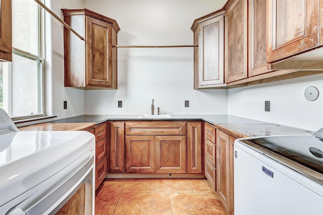 kitchen featuring washer / clothes dryer, light tile patterned flooring, a sink, range, and brown cabinets