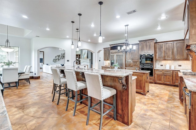 kitchen featuring visible vents, a large island, dobule oven black, arched walkways, and decorative backsplash