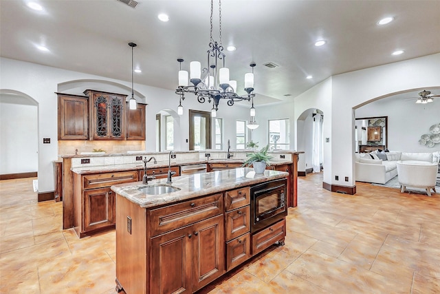 kitchen with visible vents, an island with sink, arched walkways, a sink, and black microwave