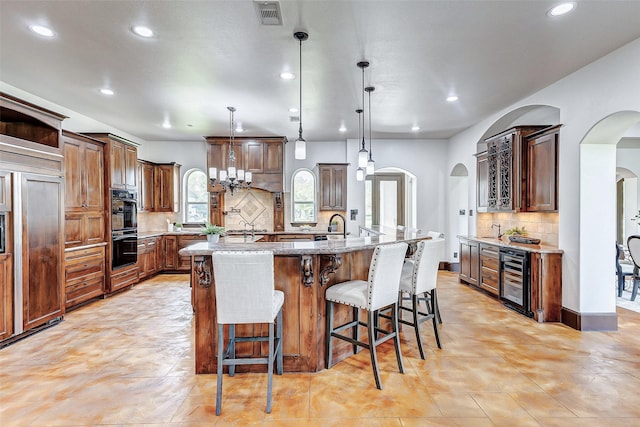 kitchen featuring a large island, light stone counters, paneled built in fridge, wine cooler, and arched walkways