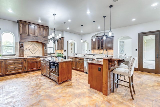 kitchen with light stone counters, a kitchen island with sink, arched walkways, a sink, and appliances with stainless steel finishes