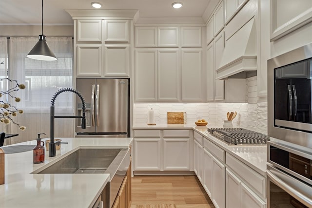 kitchen with light countertops, custom range hood, appliances with stainless steel finishes, pendant lighting, and light wood-type flooring