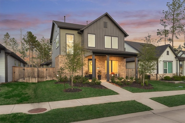 view of front facade with brick siding, board and batten siding, a front lawn, and fence