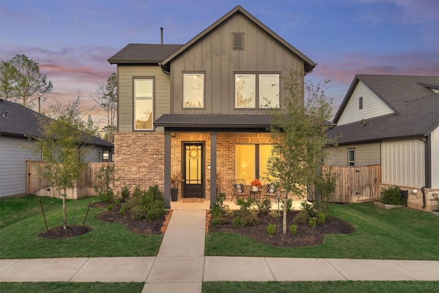 view of front facade with brick siding, board and batten siding, a yard, and fence