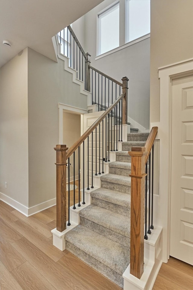 stairway with baseboards, a high ceiling, and wood finished floors