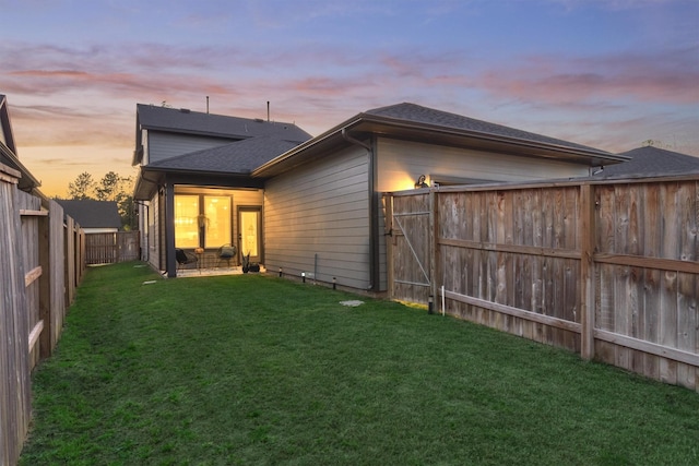 back of house at dusk featuring a yard, roof with shingles, and a fenced backyard