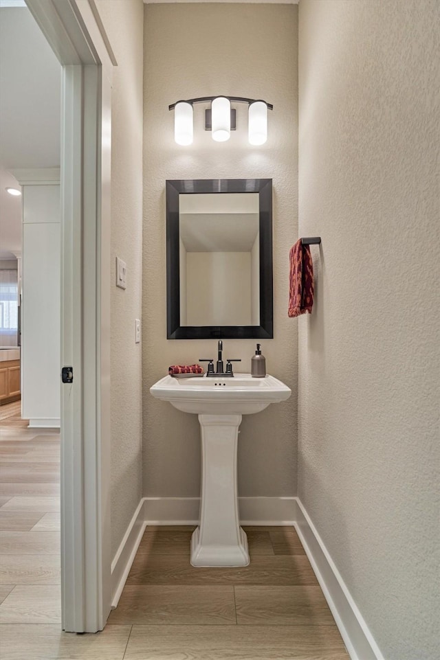 bathroom with a textured wall, baseboards, and wood finished floors