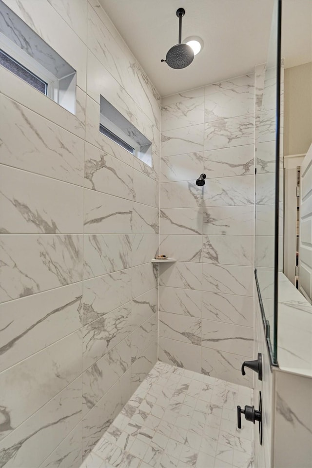 bathroom with marble finish floor and a tile shower