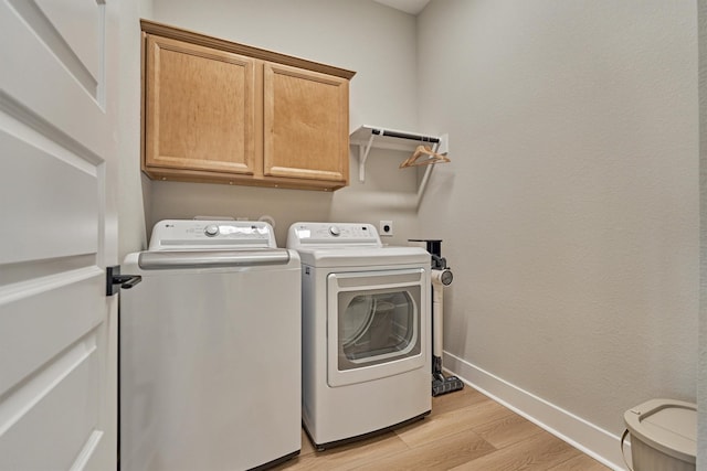 laundry area with cabinet space, light wood-type flooring, baseboards, and separate washer and dryer