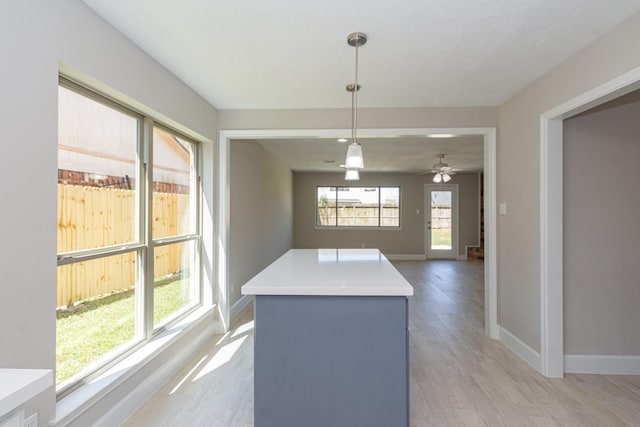 kitchen with pendant lighting, light wood-style flooring, a kitchen island, light countertops, and baseboards