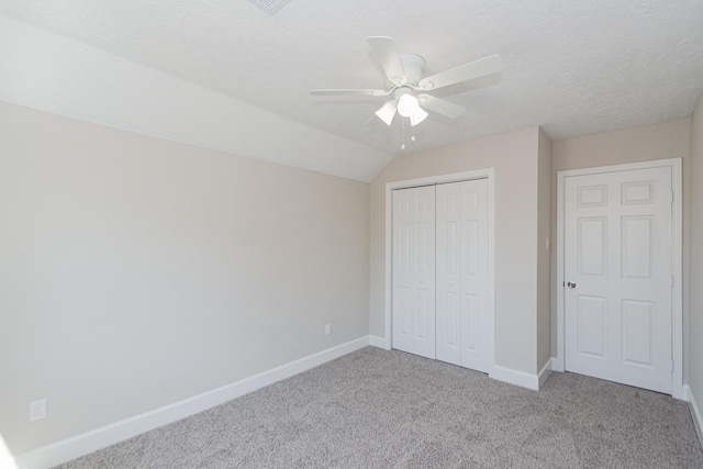 unfurnished bedroom featuring baseboards, lofted ceiling, carpet floors, a closet, and a textured ceiling