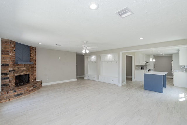 unfurnished living room with light wood-type flooring, visible vents, a ceiling fan, a sink, and a brick fireplace