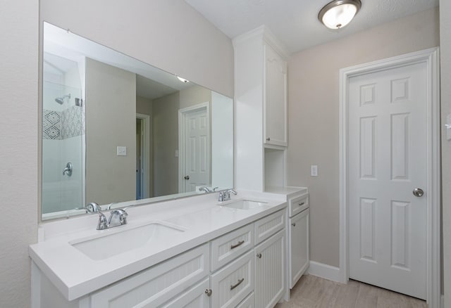 full bathroom with double vanity, wood finished floors, a tile shower, and a sink