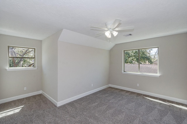 spare room with vaulted ceiling, baseboards, dark colored carpet, and a textured ceiling