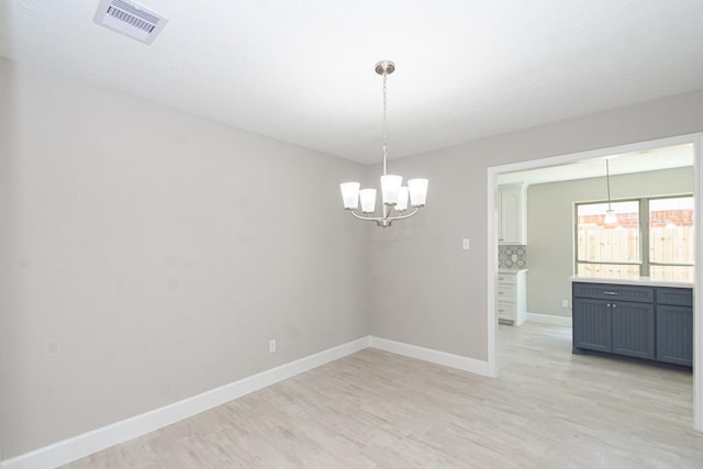 spare room with a chandelier, visible vents, light wood-style flooring, and baseboards