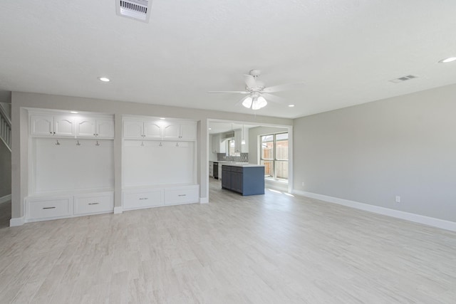 unfurnished living room with light wood-type flooring, visible vents, ceiling fan, and stairs