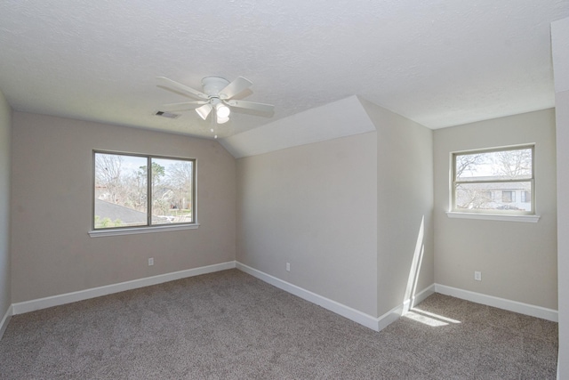 carpeted empty room featuring a wealth of natural light, visible vents, a textured ceiling, and baseboards