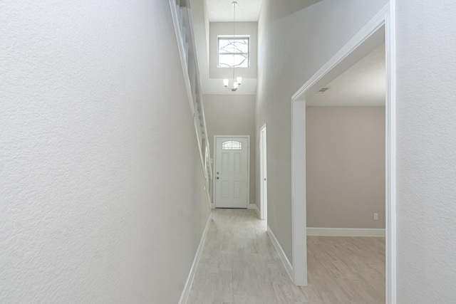 doorway to outside featuring light wood-style flooring, baseboards, and a towering ceiling