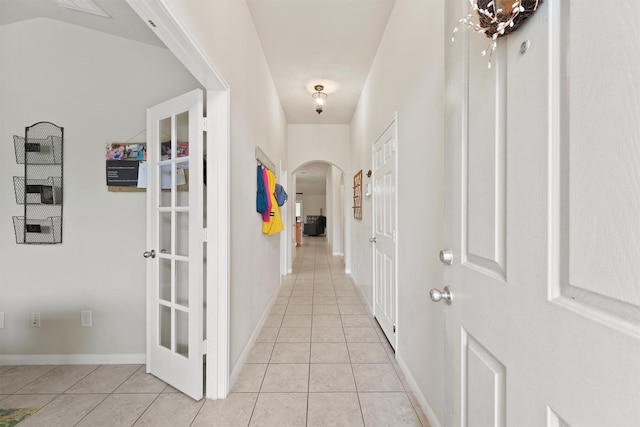 corridor featuring light tile patterned floors, baseboards, and arched walkways