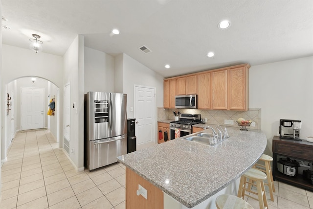 kitchen with a peninsula, arched walkways, a sink, decorative backsplash, and appliances with stainless steel finishes