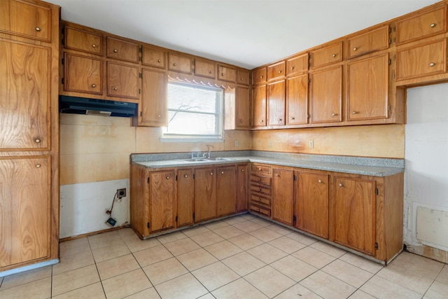 kitchen featuring under cabinet range hood, light tile patterned floors, brown cabinets, and a sink