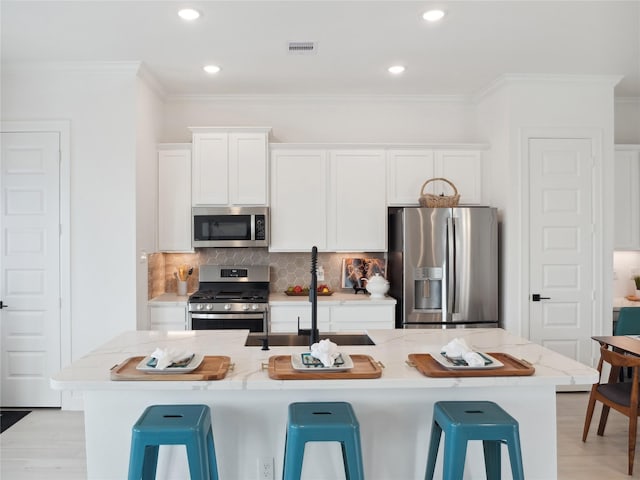 5617 Iris Harvest Dr, Houston, TX 77091 - kitchen featuring appliances with stainless steel finishes, crown molding, white cabinets, a breakfast bar area, and backsplash
