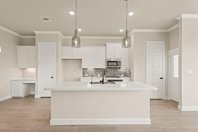 5617 Iris Harvest Dr, Houston, TX 77091 - kitchen featuring stainless steel microwave, white cabinets, crown molding, a kitchen island with sink, and tasteful backsplash