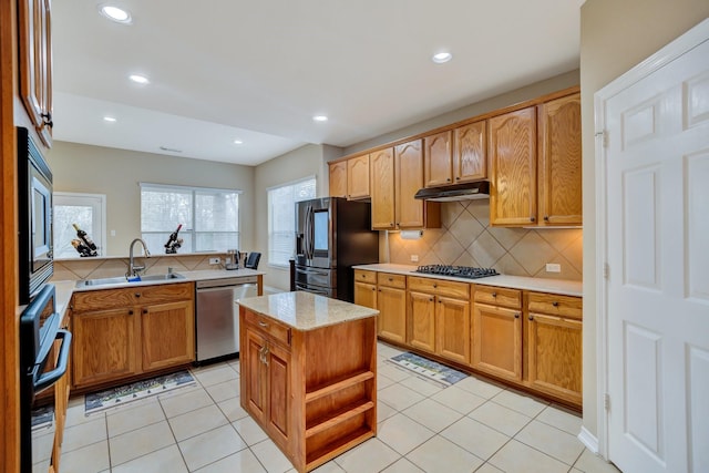 kitchen with a sink, under cabinet range hood, tasteful backsplash, stainless steel appliances, and light tile patterned floors