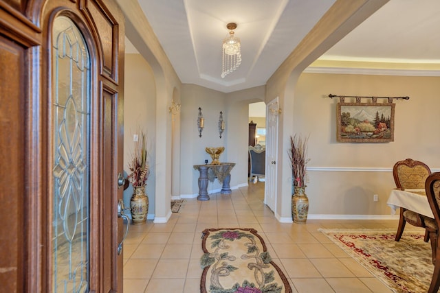 entrance foyer featuring a tray ceiling, light tile patterned floors, baseboards, and arched walkways