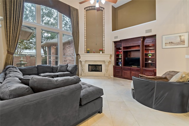 living room featuring a high ceiling, a fireplace with raised hearth, visible vents, and ceiling fan