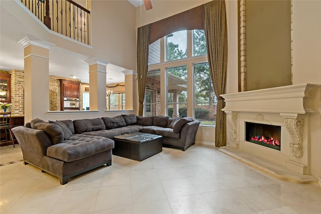 living area with decorative columns, a fireplace, a high ceiling, light tile patterned flooring, and a ceiling fan