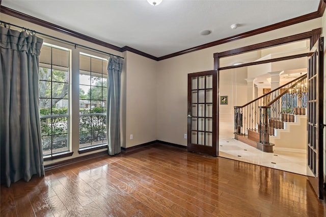 spare room with ornamental molding, wood finished floors, decorative columns, baseboards, and stairs